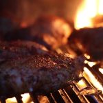 Sizzling chicken on the barbecue grill with flames in the background for a perfect summer BBQ feast