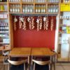 Cosy cafe corner with wooden tables, garlic, and onions hanging against a red wall, surrounded by shelves of products