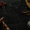 Pizza with cherry tomatoes and parsley on a dark wooden board, accompanied by flour, spoon, and fork