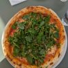 Delicious pizza topped with fresh rocket leaves served on a white plate at an outdoor café setting