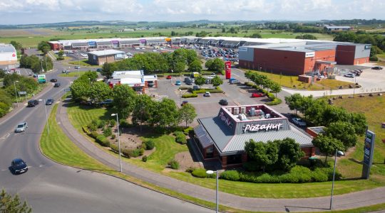 Aerial view of a retail park with popular fast food restaurants and shops, surrounded by greenery and roads