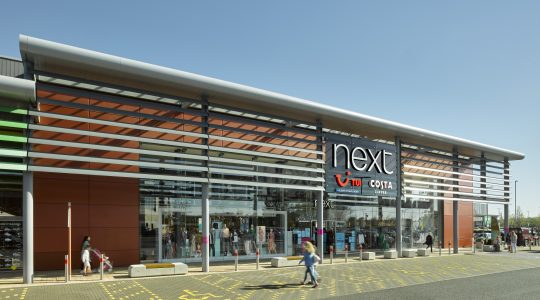 Modern retail building with Next and Costa Coffee signage, featuring large glass windows and people walking by