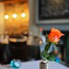 Orange rose in vase on restaurant table, warm ambient lighting in the background