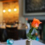 Orange rose in vase on restaurant table, warm ambient lighting in the background