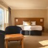 Bright hotel room with king-size bed, cosy seating area, and large window overlooking a sunny view
