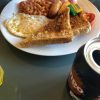 Full English breakfast with toast, egg, beans, sausage, butter, and a soft drink can on a glass table