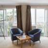 Hotel room with sea view, featuring two chairs, table, telescope, large windows, and curtains on beige carpet