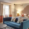 Elegant hotel room with a king-size bed, blue sofa, stylish decor, and natural light from the balcony window