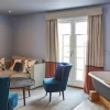 Cosy living room with blue accents, a sofa, armchairs, and a standalone bathtub near a window with curtains