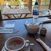 Tea set on a café table with a view of the outdoor seating area through the window, including water bottle and mask