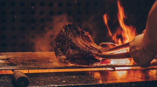 Grilled steak sizzling over open flame on a barbecue, showcasing expert cooking technique and delicious smoky flavour