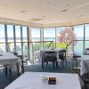 Bright restaurant interior with sea view, decorated with pink blossom tree and table settings for diners