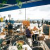 People dining at a waterfront cafe with a view of ships and a vibrant outdoor atmosphere