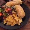 Sandwiches with crunchy tortilla chips and fresh salad on a black plate, served on a wooden table