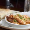 Gambas al ajillo with crusty bread on a white plate, garnished with parsley, served at a restaurant table