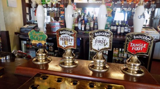 Pub bar with four beer taps, featuring Rosie's Pig, Fursty Ferret, First Call and Tangle Foot, with spirits in background