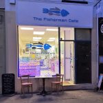 Front view of The Fisherman Café with a cosy seating area outside and glowing interior lighting