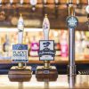 Pub bar with Flack Manor and Jurassic beer taps, including Curious Brew tap handle in a lively background setting