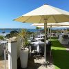 Outdoor seaside restaurant terrace with parasols, white tablecloths, and stunning ocean view on a sunny day