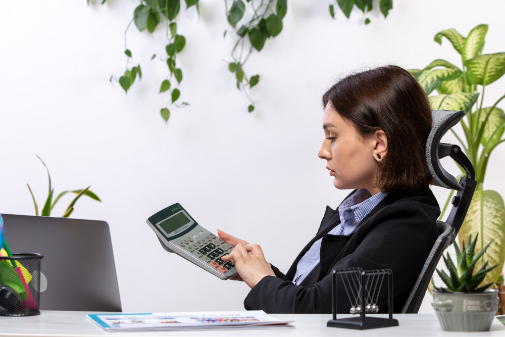 A businesswoman in a suit operates a calculator while seated at her office desk