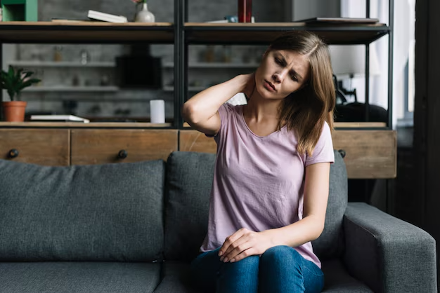 A woman sitting on a couch, resting her hands on her head, appears deep in thought or stressed