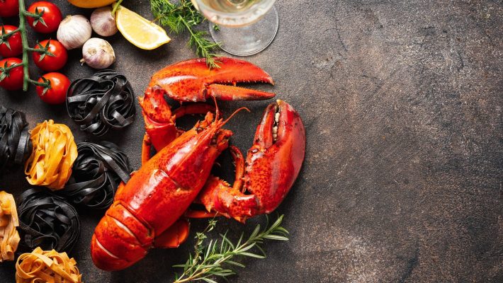 Fresh lobster with pasta, tomatoes, garlic, lemon and herbs on rustic background. Gourmet seafood meal ingredients