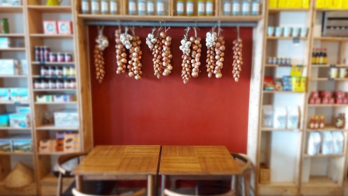 Cosy cafe corner with wooden tables, garlic, and onions hanging against a red wall, surrounded by shelves of products