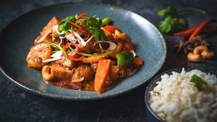Delicious Asian stir-fry with vegetables and cashews served with white rice on a dark rustic table setting
