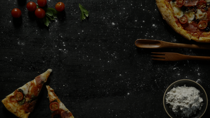 Pizza with cherry tomatoes and parsley on a dark wooden board, accompanied by flour, spoon, and fork