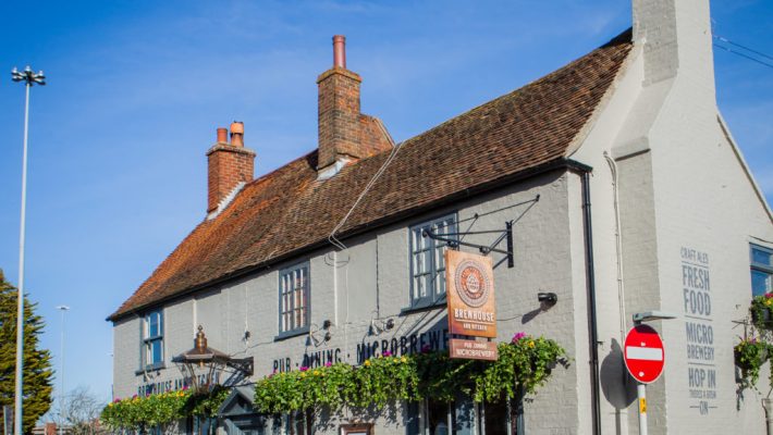 Historic English pub with hanging plants and brick chimney under a clear blue sky