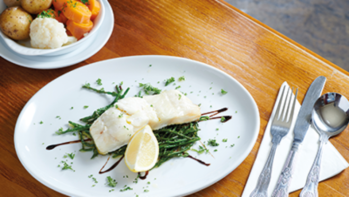 Plate of grilled fish with lemon, herbs, and balsamic glaze, served with a side of vegetables and potatoes on a wooden table