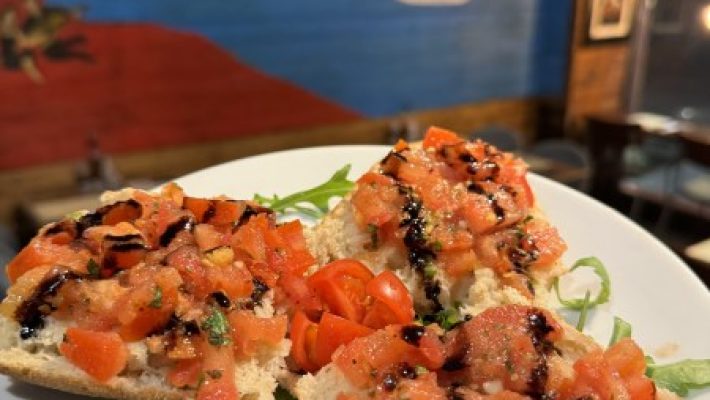 Italian bruschetta with tomatoes and balsamic glaze served on a white plate, restaurant wall art in background