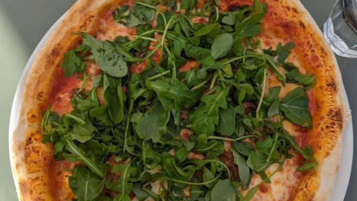 Delicious pizza topped with fresh rocket leaves served on a white plate at an outdoor café setting
