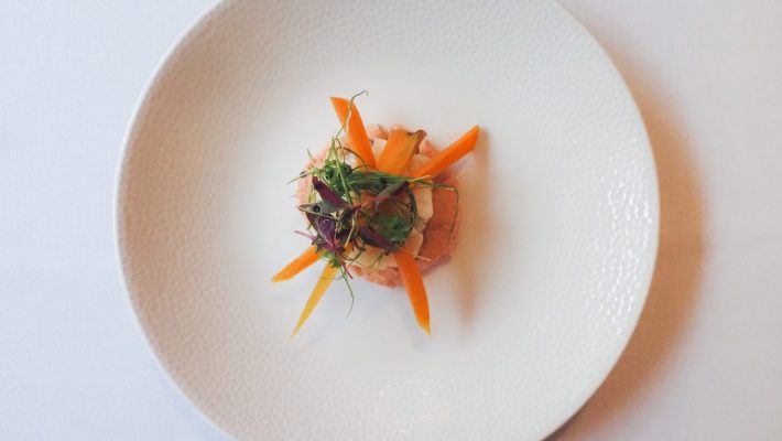 Gourmet salad with sliced carrots and microgreens elegantly presented on a white plate deconstructing fine dining