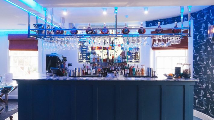 Stylish modern bar interior with illuminated blue accents, glasses on display, and an assortment of liquor bottles