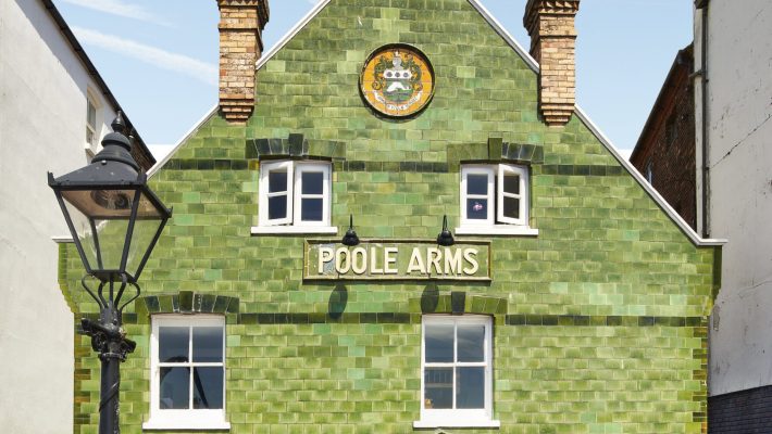 Historic green-tiled facade of Poole Arms pub with outdoor benches and signage under a clear blue sky