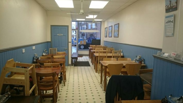 Cosy, empty café interior with wooden tables and blue accents, awaiting customers in a quaint neighbourhood setting
