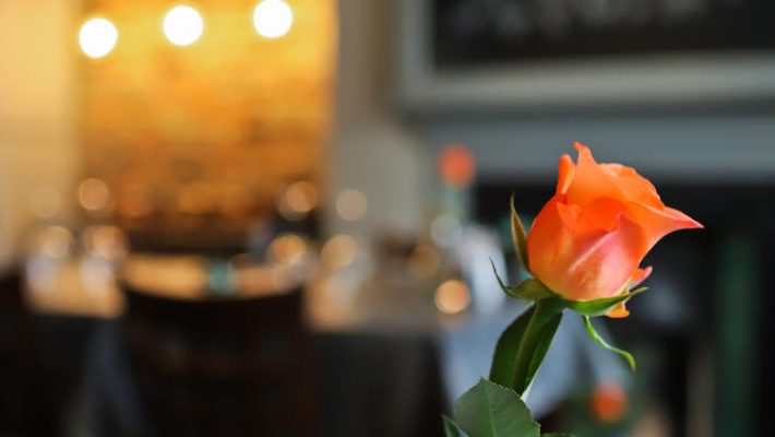 Orange rose in vase on restaurant table, warm ambient lighting in the background