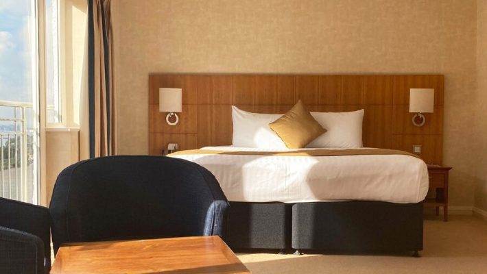 Bright hotel room with king-size bed, cosy seating area, and large window overlooking a sunny view