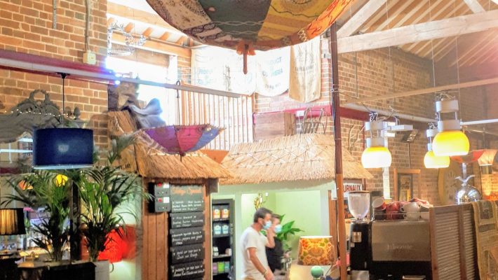 Cosy café interior with colourful decor, wooden beams, and customers enjoying drinks at a communal table in rustic setting