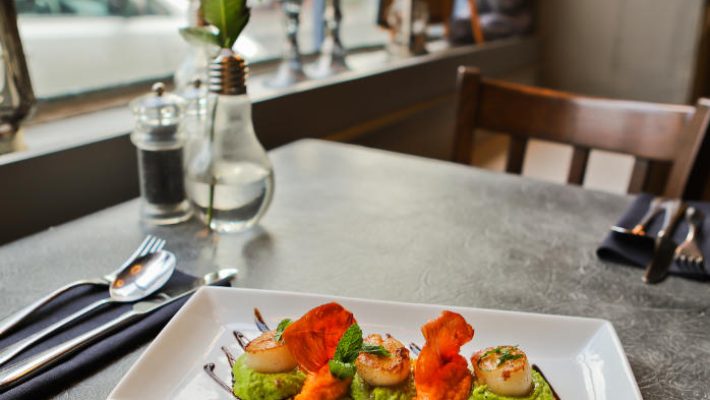 Gourmet scallops on avocado puree garnished with herbs and crispy toppings in cosy restaurant setting