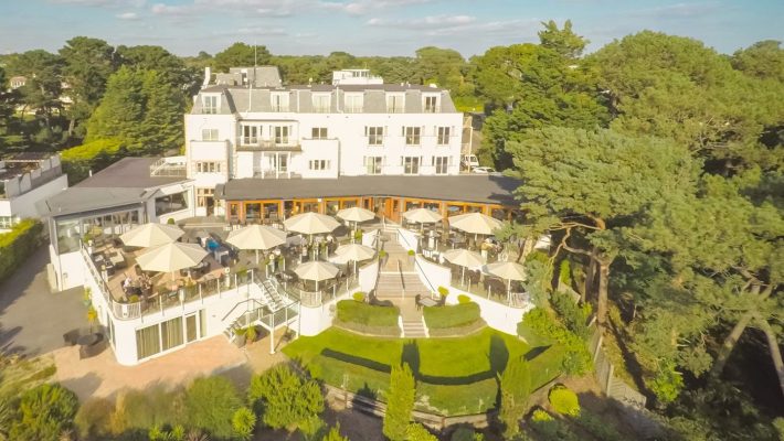 Aerial view of a luxury hotel with outdoor terraces, surrounded by lush greenery and blue skies