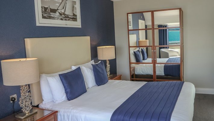 Elegant hotel room with double bed, navy accents and mirrored wardrobe, creating a spacious and serene atmosphere