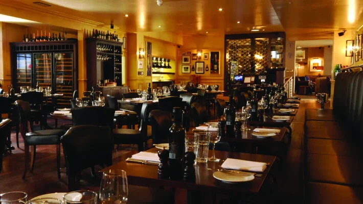 Elegant restaurant interior with neatly set tables, dim lighting, and wine displays, creating a cosy dining atmosphere