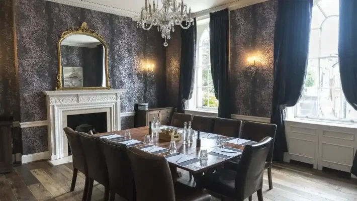 Elegant dining room with chandelier, ornate mirror, large table set for a meeting, dark wallpaper and curtains