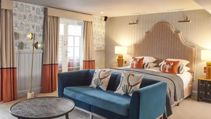 Elegant hotel room with a king-size bed, blue sofa, stylish decor, and natural light from the balcony window