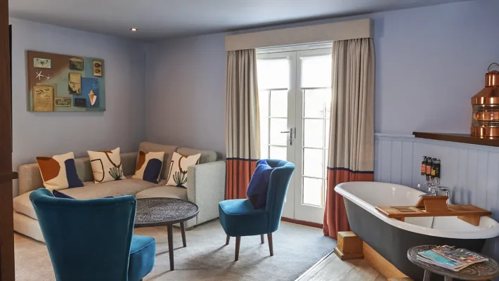 Cosy living room with blue accents, a sofa, armchairs, and a standalone bathtub near a window with curtains