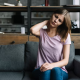 A woman sitting on a couch, resting her hands on her head, appears deep in thought or stressed