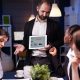 A man presents to an audience, engaging them with visual aids and discussion during a professional meeting