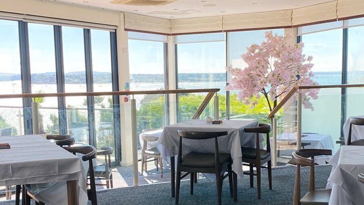 Bright restaurant interior with sea view, decorated with pink blossom tree and table settings for diners